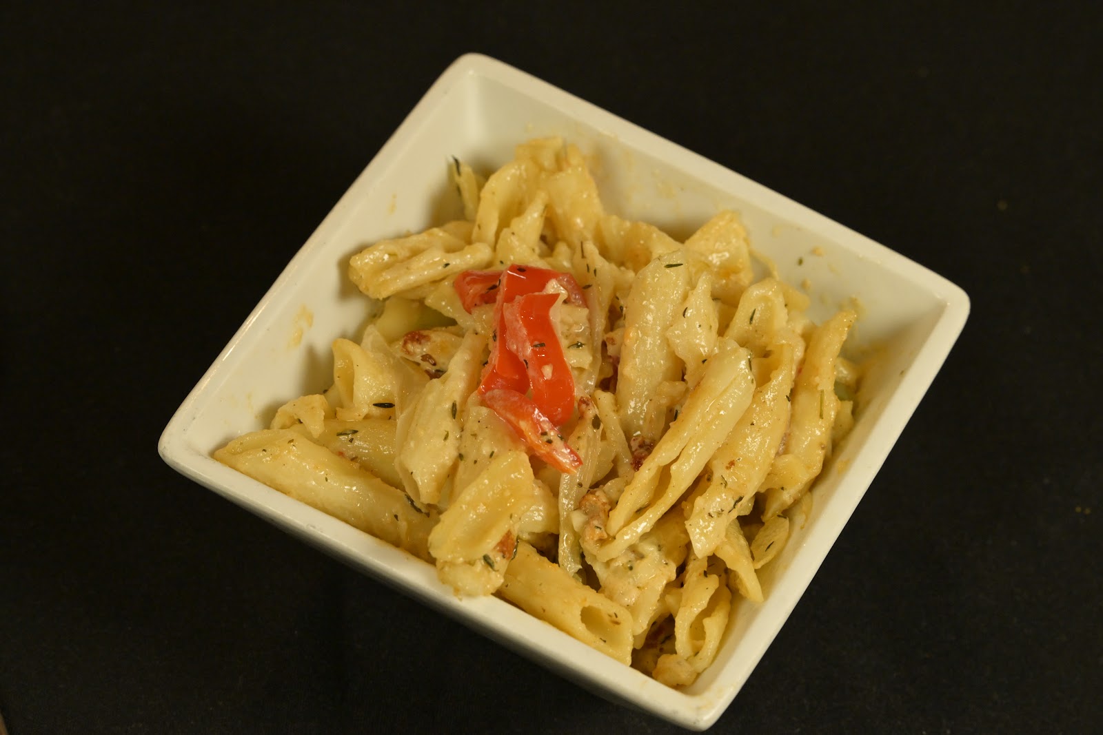 Penne pasta with red peppers in a square bowl